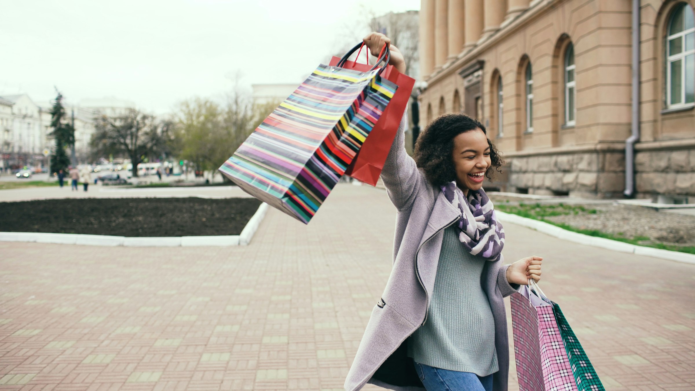 A woman laughing and holding up colorful shopping bags on a city street